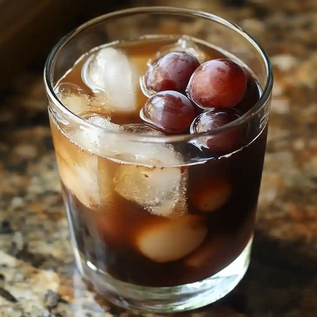 Refreshing grape soda with ice cubes in a glass on a rustic wooden surface.