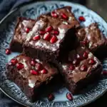 Decadent chocolate brownies topped with pomegranate seeds on a decorative black and white plate. Perfect for sweet craving, dessert, or special occasion. Rich, chewy, and chocolatey.
