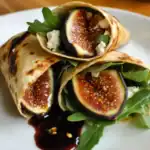 Sweet fig wraps with goat cheese, fresh arugula, and balsamic glaze on a white plate. Delicious and healthy vegetarian appetizer or snack from Station Recipes.