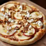 Creamy pear and walnut pizza topped with crumbled cheese and caramelized walnuts, served on a rustic wooden board, perfect for cozy family dinners and comfort food cravings.