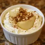 Creamy pear dessert topped with walnuts and a sprinkle of cinnamon in a white ramekin.