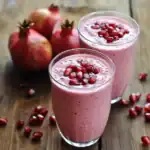 Refreshing pomegranate smoothie in tall glasses garnished with pomegranate seeds, with whole pomegranates in the background, perfect for healthy fruit recipes.