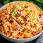 Crispy carrot slaw with dried cranberries and chopped pecans in a creamy dressing, perfect for healthy side dishes or picnic recipes.