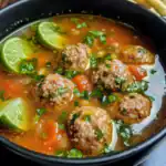 Savory Mexican meatball soup with lime wedges, cilantro, and vegetables in broth, traditional dish from Station Recipes.