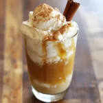 Rich caramel and vanilla ice cream float topped with whipped cream, cinnamon, and a cinnamon stick on a wooden surface. Perfect for dessert or a sweet treat.