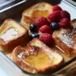 Fresh French toast topped with berries and powdered sugar, served with syrup, perfect for breakfast or brunch.