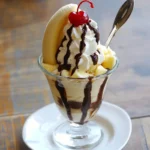Sweet banana split sundae with whipped cream, chocolate drizzle, maraschino cherry, and vanilla ice cream served in a glass, perfect for dessert recipes and summer treats.
