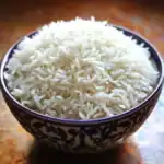 Fluffy cooked white rice in decorative bowl, perfect side dish, Asian cuisine, steaming hot, plain cooked rice, staple food, healthy carbohydrate, rice bowl, food photography, rice served in traditional bowl, rustic kitchen setting, home-cooked rice, easy side dish, nutritious staple, close-up of rice grains.