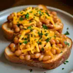 Savory baked beans on toasted bread topped with shredded cheddar cheese and chopped herbs. A hearty, delicious breakfast or snack option from Station Recipes.