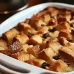 Golden brown bread pudding with raisins in a white baking dish, topped with a caramelized crust. perfect comfort food recipe, easy dessert ideas, and variations for all occasions.