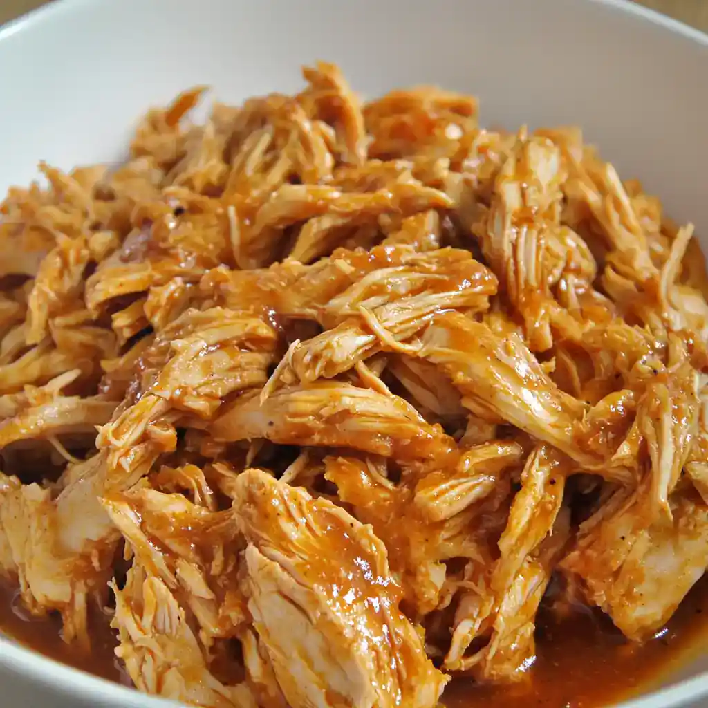 Tender shredded chicken in savory BBQ sauce in a bowl, ready for sandwiches or meal prep, perfect for easy and delicious recipes from Station Recipes.