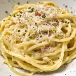 Creamy Alfredo pasta with grated Parmesan, black pepper, and fresh herbs on top, served on a white plate. Perfect comfort food recipe for pasta lovers.