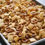 Crunchy snack mix with pretzels, cereal, and nuts in a baking dish for easy serving.