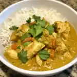Creamy chicken curry served with white rice, garnished with fresh cilantro, featuring tender chicken pieces in a flavorful, spiced sauce. Perfect for a comforting meal.