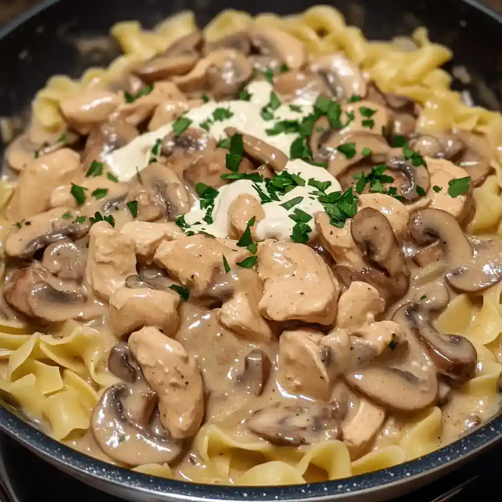 Savory chicken and mushroom stroganoff served over egg noodles with fresh herbs, creamy sauce, and tender chicken pieces perfect for a comforting dinner.