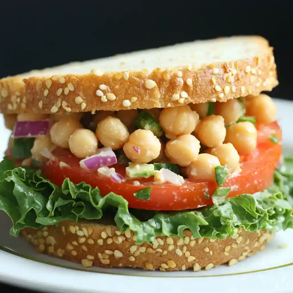 Fresh chickpea sandwich with tomato, lettuce, and onion on whole grain bread, healthy vegan lunch idea. Perfect for quick, nutritious meals and plant-based diet options.