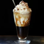 Creamy iced coffee drink topped with whipped cream and chocolate shavings, featuring caramel drizzle, served in a tall glass with a straw. Perfect for coffee lovers seeking a sweet, indulgent beverage.