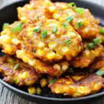 Golden crispy corn fritters topped with green onions, served in a black skillet, perfect for savory snack recipes.