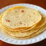 Fresh homemade corn tortillas stacked on a white plate, perfect for traditional Mexican dishes.