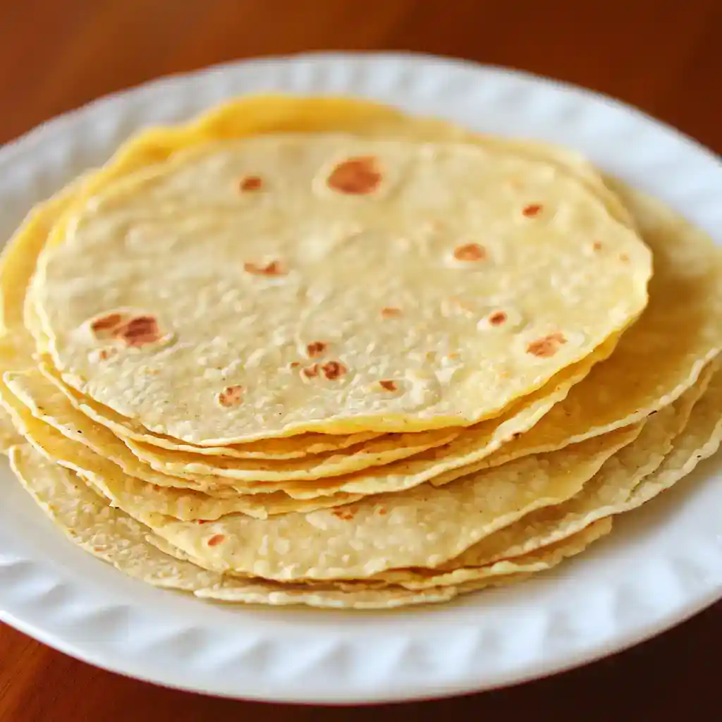 Fresh homemade corn tortillas stacked on a white plate, perfect for traditional Mexican dishes.