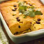 Cheese and Black Bean Corn Casserole baked dish with fresh cilantro and chopped green onions, made with cheesy, creamy cornmeal batter, perfect for a hearty, flavorful meal or side dish.