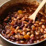 Creamy and hearty bean chili in a pot with a wooden spoon, ready for serving. Perfect comfort food recipe from Station Recipes, filled with mixed beans, vegetables, and rich spices.