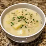 Creamy potato soup with chives in a white bowl on a granite countertop.