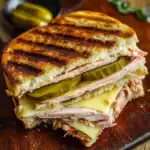 Grilled chicken and cheese melt sandwich with pickles on toasted bread, served on a wooden cutting board. Perfect for lunch or a quick snack, featuring melty cheese and crispy grill marks.