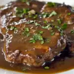 Juicy, tender beef steak covered in rich brown gravy, garnished with freshly chopped parsley, served on a white plate — a hearty homemade station-inspired recipe.