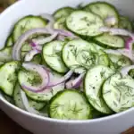 Cucumber and red onion salad with fresh dill, seasoned with black pepper and herbs, served in a white bowl, perfect for light, healthy meals and side dishes.