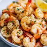 Succulent garlic butter shrimp with black pepper and fresh herbs on a white plate, garnished with lemon wedges, perfect for seafood lovers and easy weeknight dinners, from Station Recipes.