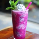 Creamy dragon fruit smoothie with fresh mint and a pink straw, perfect for summer refreshment. Made with vibrant pink dragon fruit, ice, and plant-based ingredients for a healthy, colorful treat.