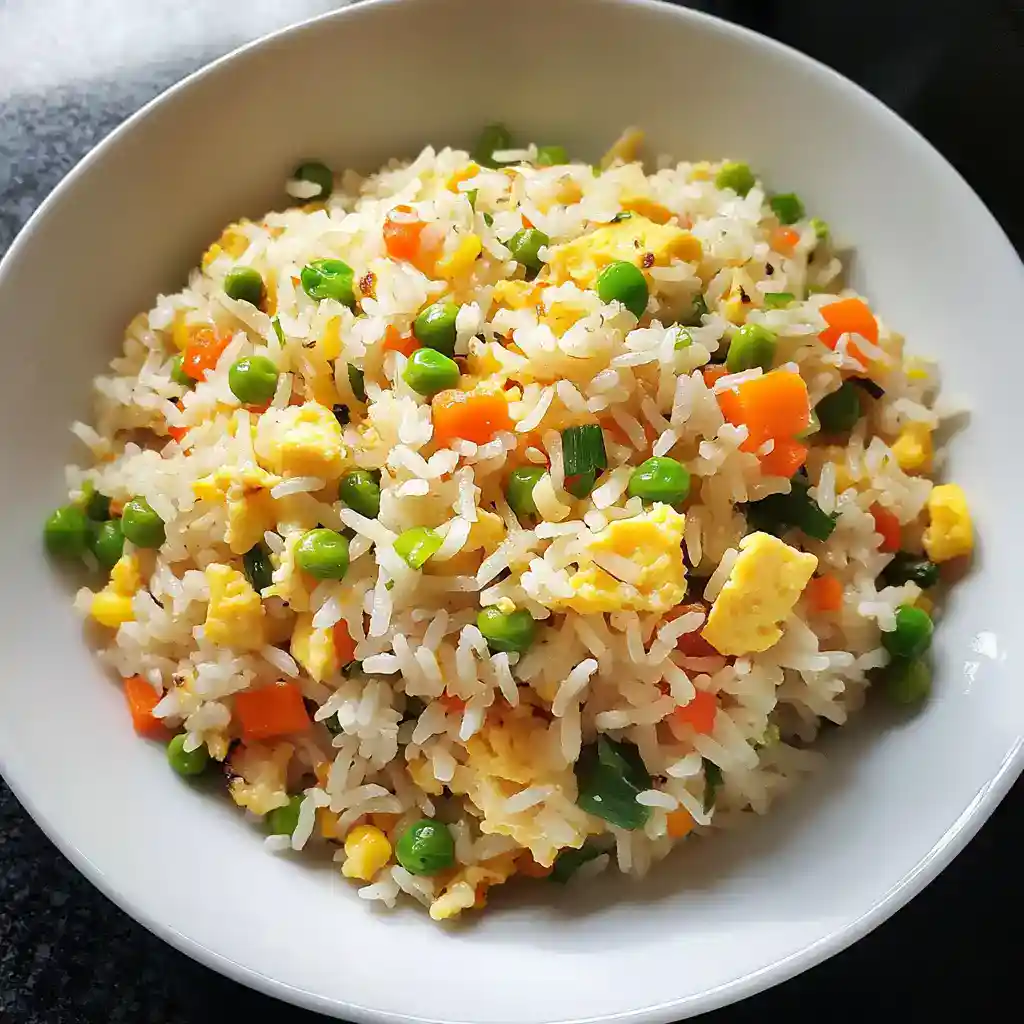 Steamed vegetable fried rice with peas, carrots, corn, and scrambled eggs, served in a white bowl. Perfect for quick, healthy meals and easy to prepare at home with simple ingredients.