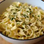 Butter and garlic coated fettuccine pasta garnished with parsley in a white bowl for a simple, flavorful pasta recipe.