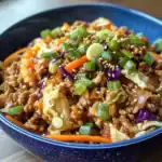 Stir-fried ground beef with vegetables topped with scallions, sesame seeds in a blue bowl, delicious Asian-inspired dish.