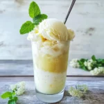 Creamy vanilla ice cream sundae with fresh mint garnish in a tall glass on wooden table. Perfect dessert recipe from Station Recipes.