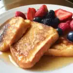 Sweet French toast with fresh mixed berries on a white plate, topped with syrup, perfect for a delicious breakfast or brunch.