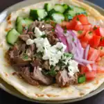 Slow Cooker Beef Gyro with Fresh Vegetables on Flatbread, Greek-inspired dish, easy homemade gyro recipe, delicious beef gyro sandwich, healthy meal with cucumber, tomato, onion, and feta cheese.