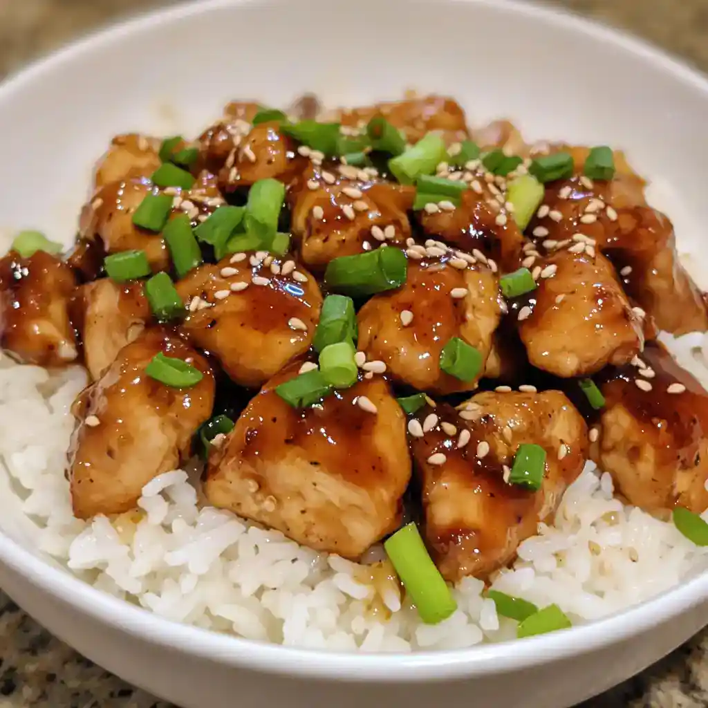 Succulent chicken bites glazed with teriyaki sauce, served over steamed white rice, garnished with chopped green onions and sesame seeds for a flavorful Asian-inspired dish.