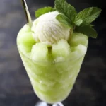 Cool green melon slush with a scoop of vanilla ice cream, fresh mint garnish, served in a tall glass, perfect summer dessert.