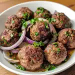 Juicy homemade meatballs with herbs and spices, served with sliced red onions and fresh parsley in a savory sauce, perfect for Italian-inspired meals or comfort food.