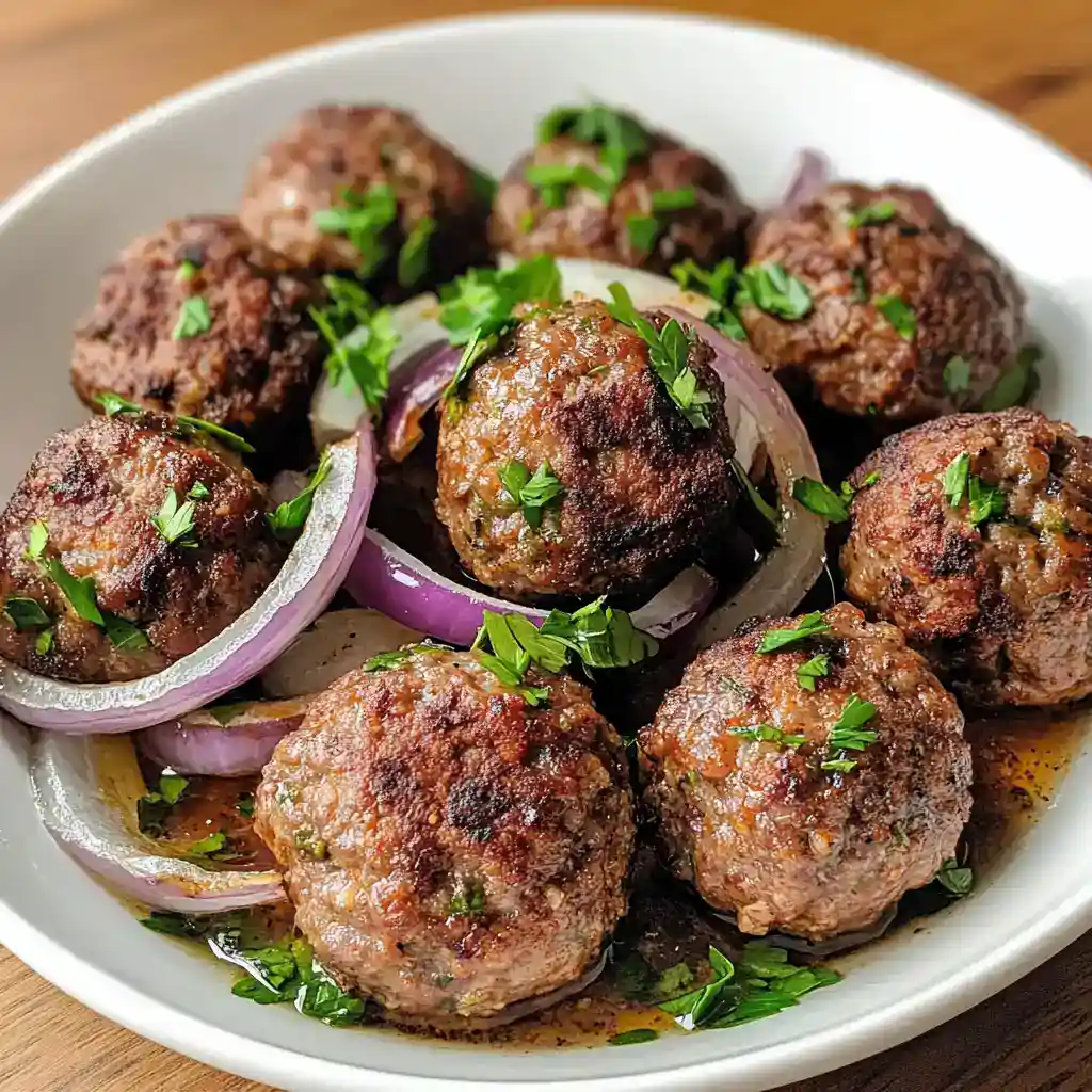 Juicy homemade meatballs with herbs and spices, served with sliced red onions and fresh parsley in a savory sauce, perfect for Italian-inspired meals or comfort food.