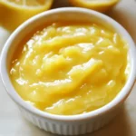 Sweet lemon curd in a ramekin, ready for dessert or spreading. Perfect for adding flavor to cakes, tarts, or toast with its vibrant citrus taste. A delicious and tangy homemade lemon dessert.