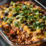 Hearty beef taco casserole with black beans, corn, cheese, and fresh cilantro in a glass baking dish. A flavorful, baked Mexican-inspired dish perfect for easy weeknight dinners or family gatherings.