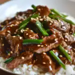 Sautéed beef with green onions and sesame seeds drizzled in savory sauce served over white rice - a delicious Asian-inspired meal.