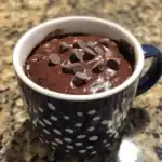 Rich chocolate mug cake topped with chocolate chips on a speckled granite countertop.