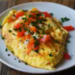 Crispy breakfast omelette garnished with fresh herbs, diced tomatoes, and parsley, served on a white plate for a hearty morning meal.