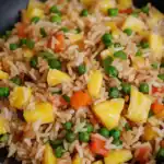 Crispy pineapple fried rice with mixed vegetables, green peas, and colorful bell peppers served in a skillet. Perfect for quick, delicious Asian-inspired meals.