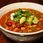 Creamy, hearty chili with kidney beans, ground meat, fresh avocado, and cilantro garnished, served in a white bowl, perfect for warming up and enjoying authentic comfort food.