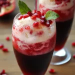 Sweet pomegranate cocktail with fresh mint garnish, served over ice with a frosty appearance. Perfect for summer drinks, featuring vibrant red pomegranate seeds and icy coolness for a refreshing beverage.